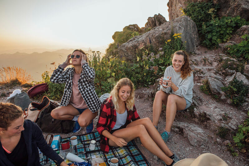 friends enjoying picnic together after hiking in the mountain