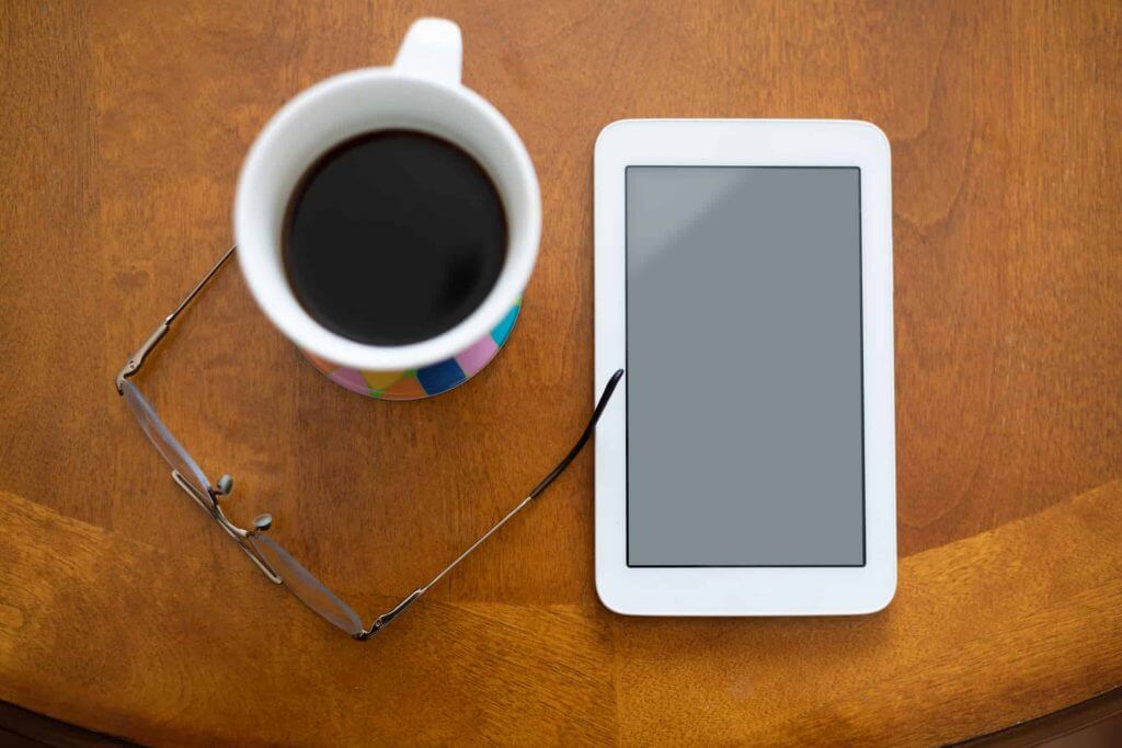 a cup of coffee, tablet and a pair of eye glasses, placed on a table