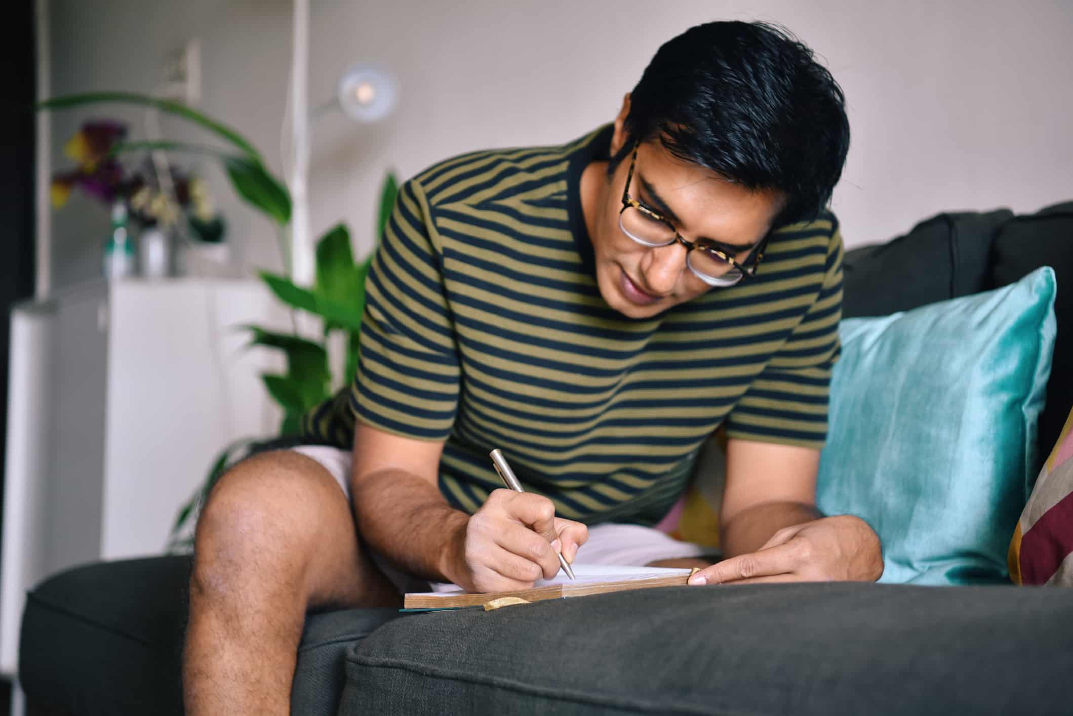 man writing down something while sitting on a sofa